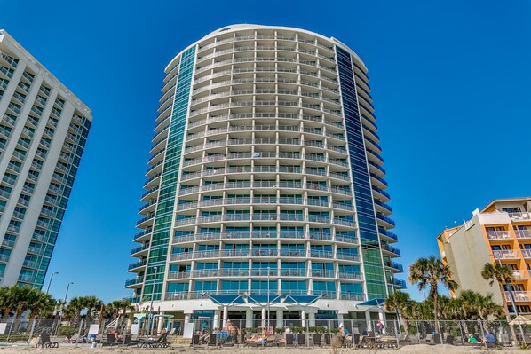 A multi-story hotel with balconies, a pool area, and a beach view.