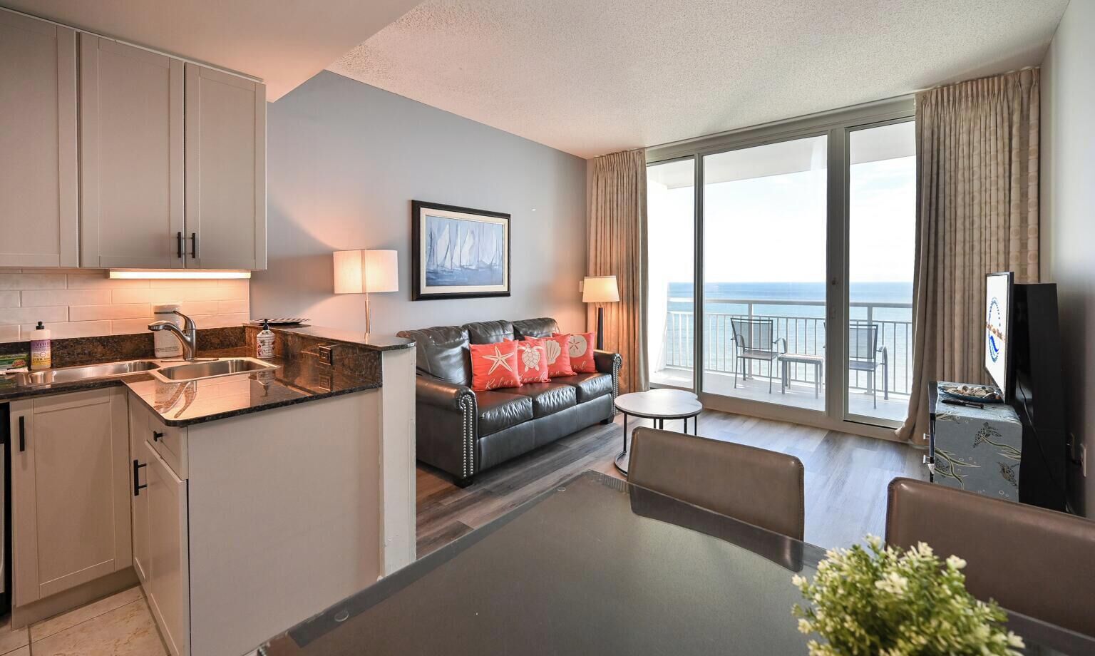 A hotel room with a kitchen, a sofa, a dining table, a TV, and a balcony with a view.