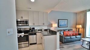 A compact kitchen with a microwave, oven, and dishwasher, a dining area with a table and a sofa, and a window with curtains. - Fabulous Penthouse, Central MB, 2 Balconies,Watch Sunrise in Your Bed (Myrtle Beach)