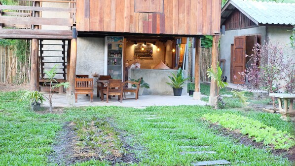 Un edificio de madera rústico con un área de estar al aire libre techada, plantas en macetas y un pequeño jardín.