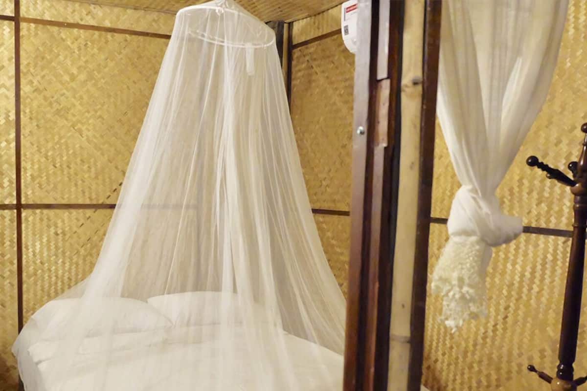 A room with a bed under a white canopy, a wooden nightstand, and a wall with a woven pattern.