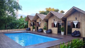 A poolside area with wooden huts, each with a thatched roof and a small window. There are bean bags and potted plants around the huts. - Lanna House Lanna Hut Chiangmai (San Kamphaeng)