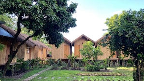 A row of thatched-roof huts with a garden in the foreground. - Lanna House Lanna Hut Chiangmai (San Kamphaeng)