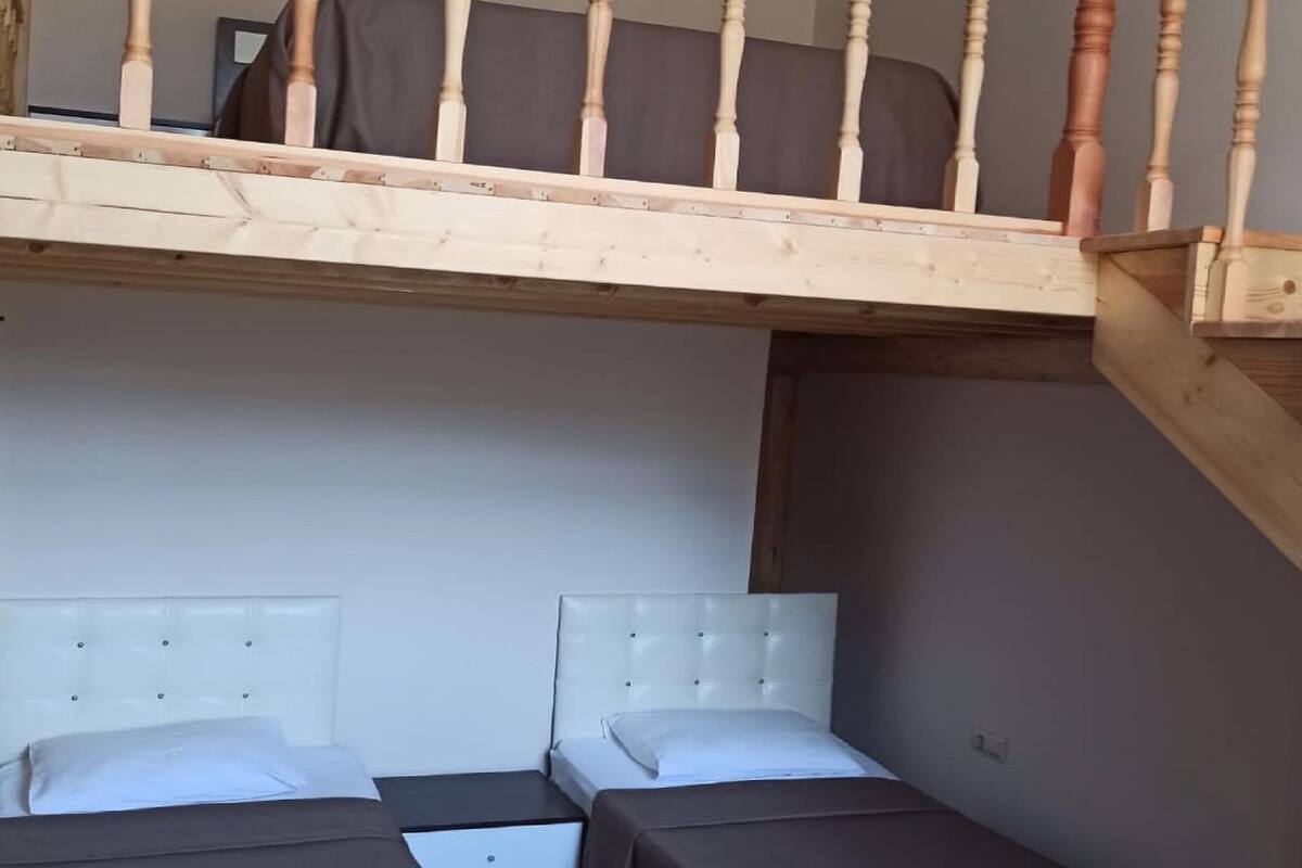 A loft-style bedroom with a wooden staircase, two beds, and a small table.