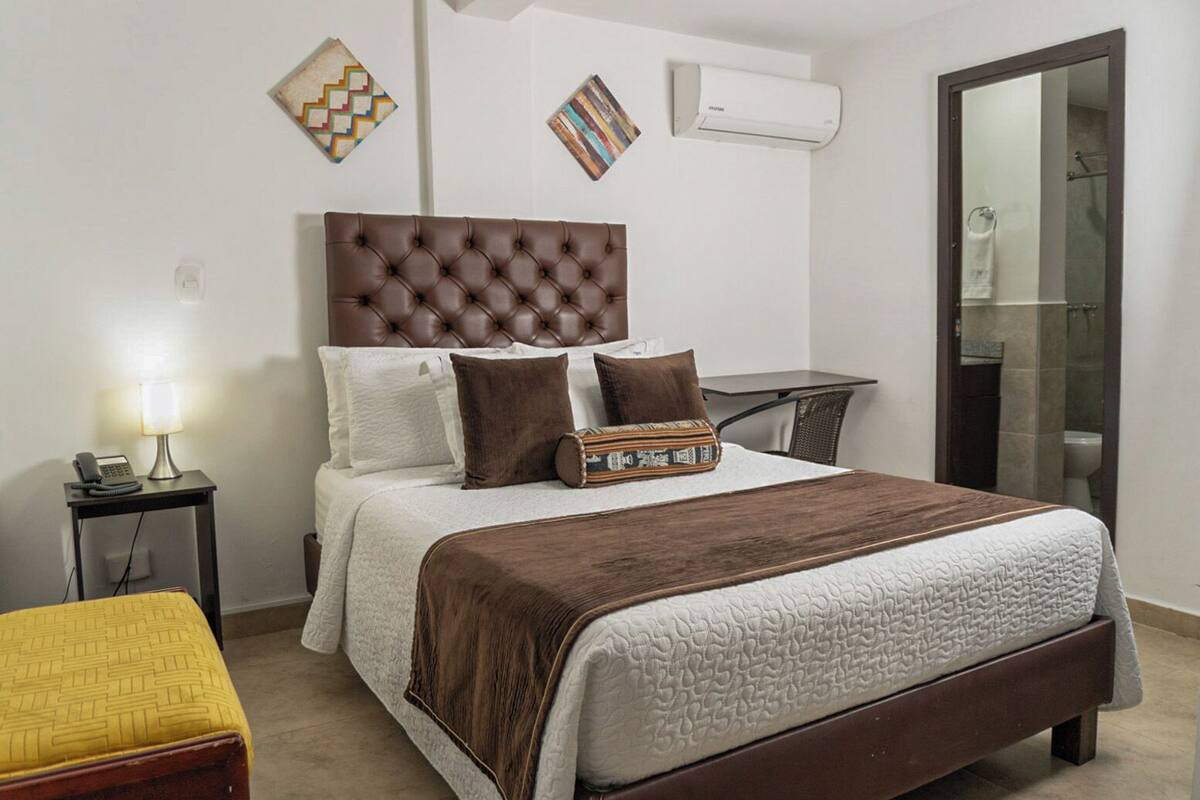A neatly arranged bedroom with a large bed, bedside tables, a bedside lamp, and a small table with a telephone.