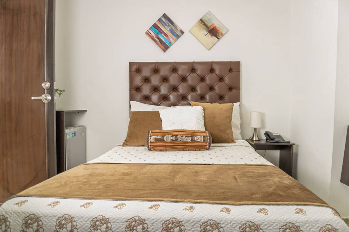 A neatly made bed with a brown headboard, a patterned bedspread, and a decorative pillow. There are two framed artworks on the wall above the bed.