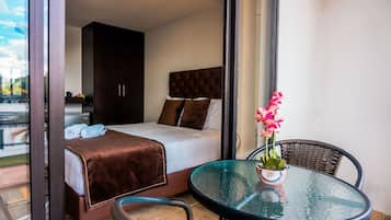 Habitación de hotel con cama, una mesita de vidrio con planta y vista al exterior.