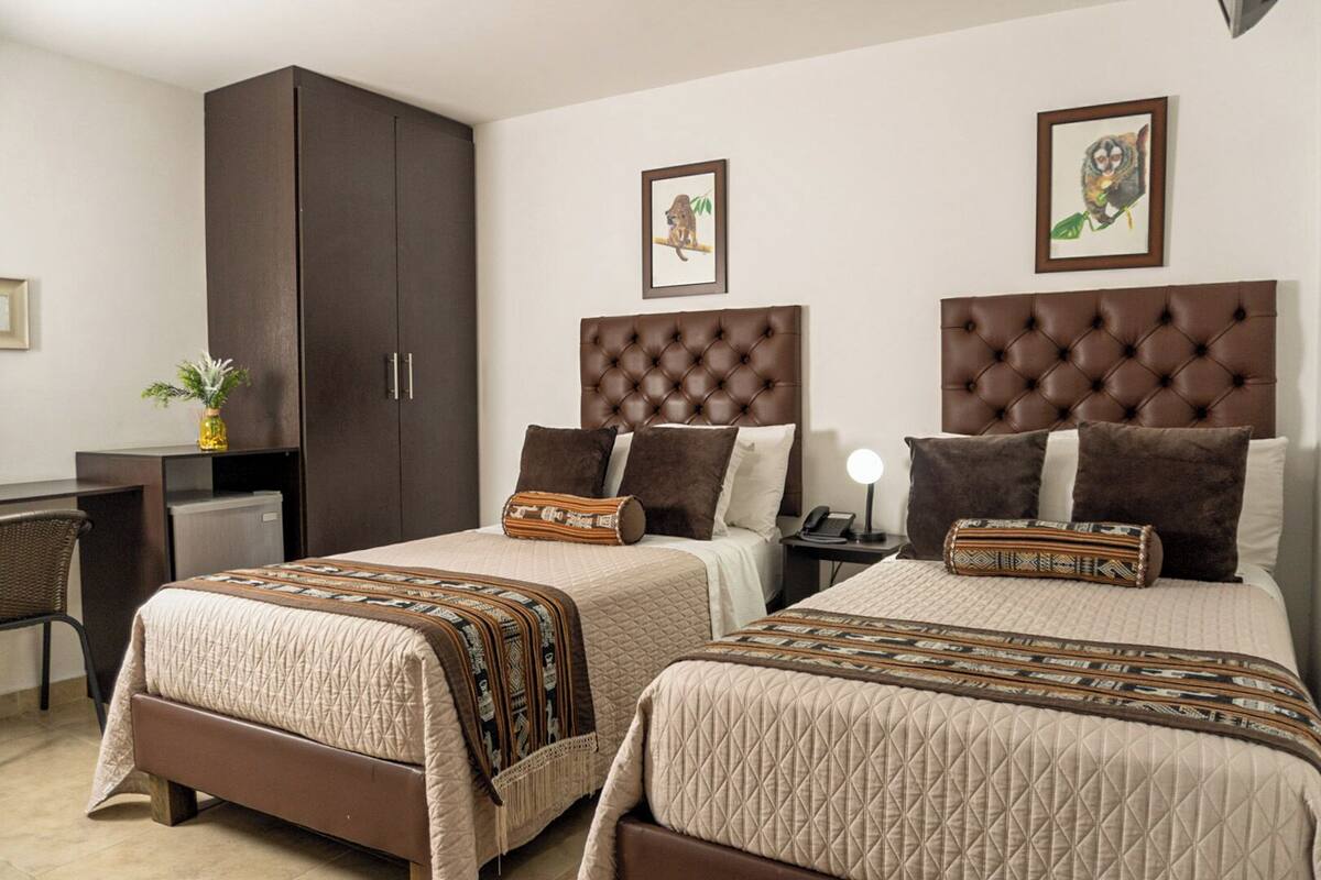 A hotel room with two queen beds, dark wooden wardrobe, and a desk with a chair.