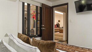 Um quarto com uma cama, uma porta de madeira e uma televisão fixada na parede.