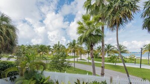 A pool with a white fence, palm trees, and a view of the beach.