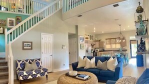 A spacious living room with a staircase, a blue sofa, and a woven ottoman. - Lagoon Front, Fire Pit, Quiet, Nature ~ Otter Cove (Indian Pass)