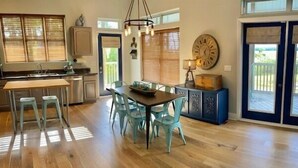 A spacious kitchen with a dining area, wooden flooring, and large windows. - Lagoon Front, Fire Pit, Quiet, Nature ~ Otter Cove (Indian Pass)
