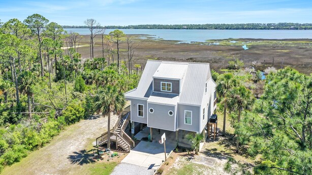 A two-story house with a covered porch, surrounded by dense vegetation and a view of a large body of water. - Lagoon Front, Fire Pit, Quiet, Nature ~ Otter Cove (Indian Pass)