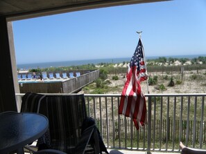 A balcony with a view of the beach, an American flag, and a pool area.