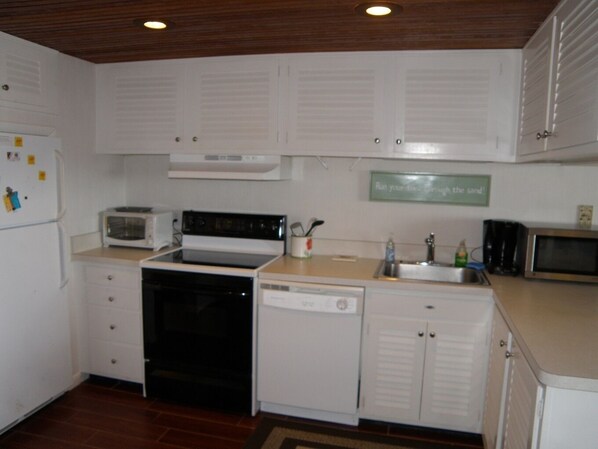 A compact kitchen with white cabinets, a stove, microwave, and dishwasher.
