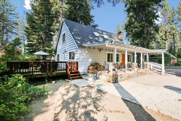 Une maison à deux étages avec un porche, une terrasse en bois et une cheminée en pierre.