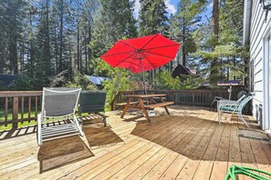 Eine Holzterrasse mit Picknicktisch und -stühlen, einem roten Sonnenschirm und Blick auf ein bewaldetes Gebiet.