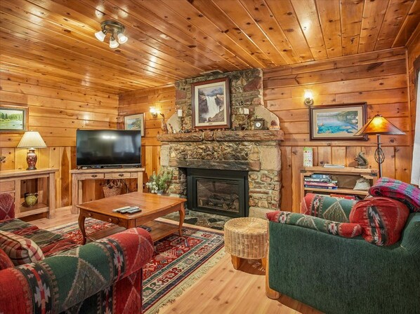 Una sala de estar acogedora con chimenea de piedra, paredes de madera, un televisor de pantalla plana y asientos cómodos.
