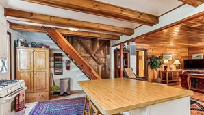 Una cocina con vigas de madera, estufa, armarios y un comedor con mesa y sillas.