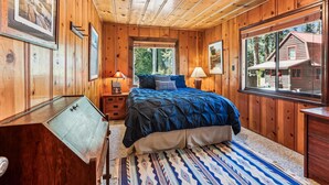 Un dormitorio acogedor tipo cabaña de madera con una cama grande, un escritorio y una ventana que ofrece vistas al exterior.