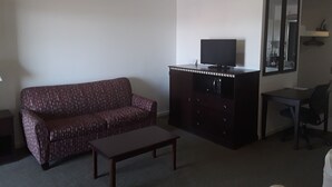 A living room with a patterned sofa, a dark wooden cabinet with a television on top, a small table, and a chair. - Italy Inn (Italy)