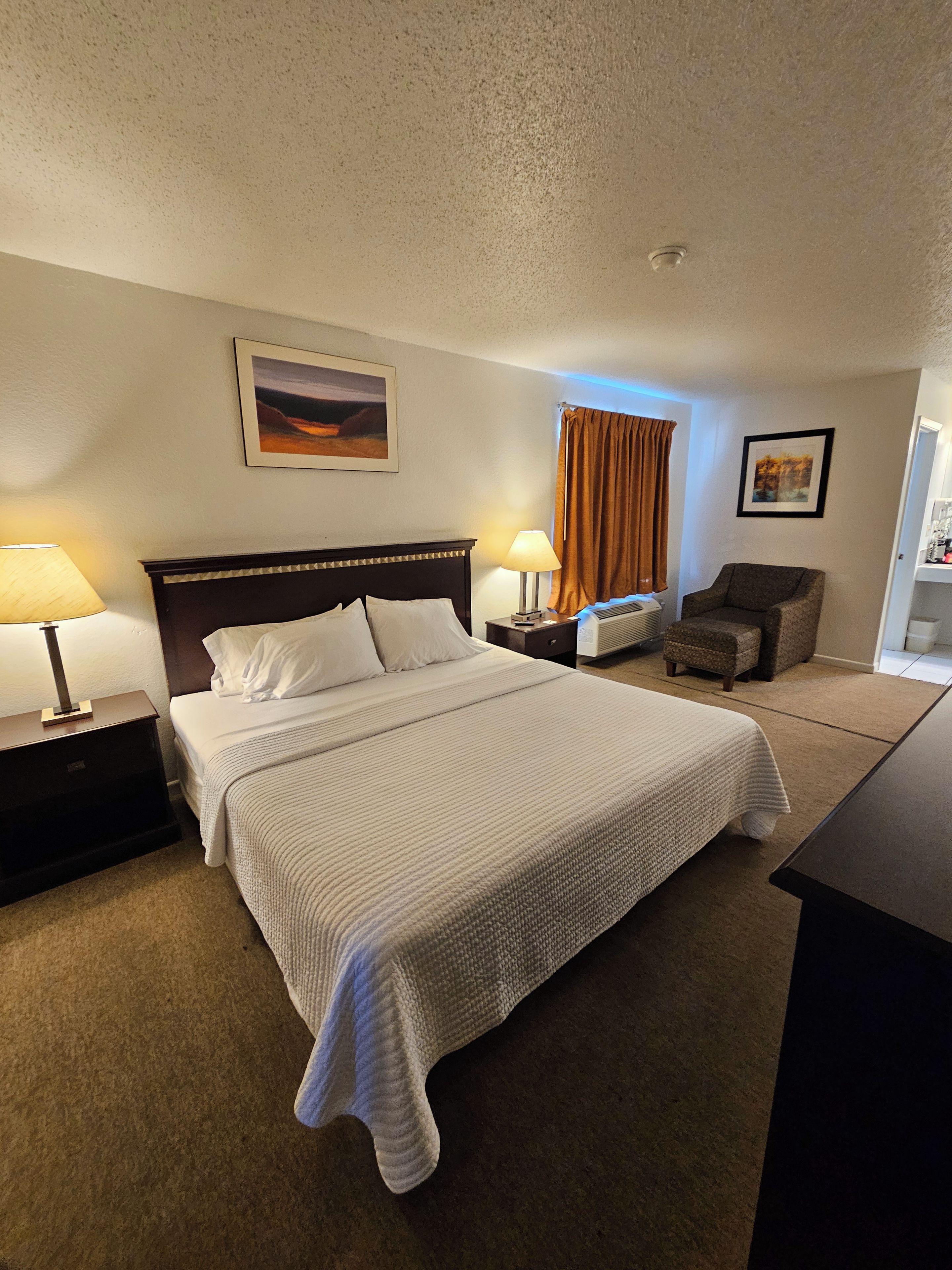 A hotel room with a bed, two bedside tables with lamps, a chair, and a desk.