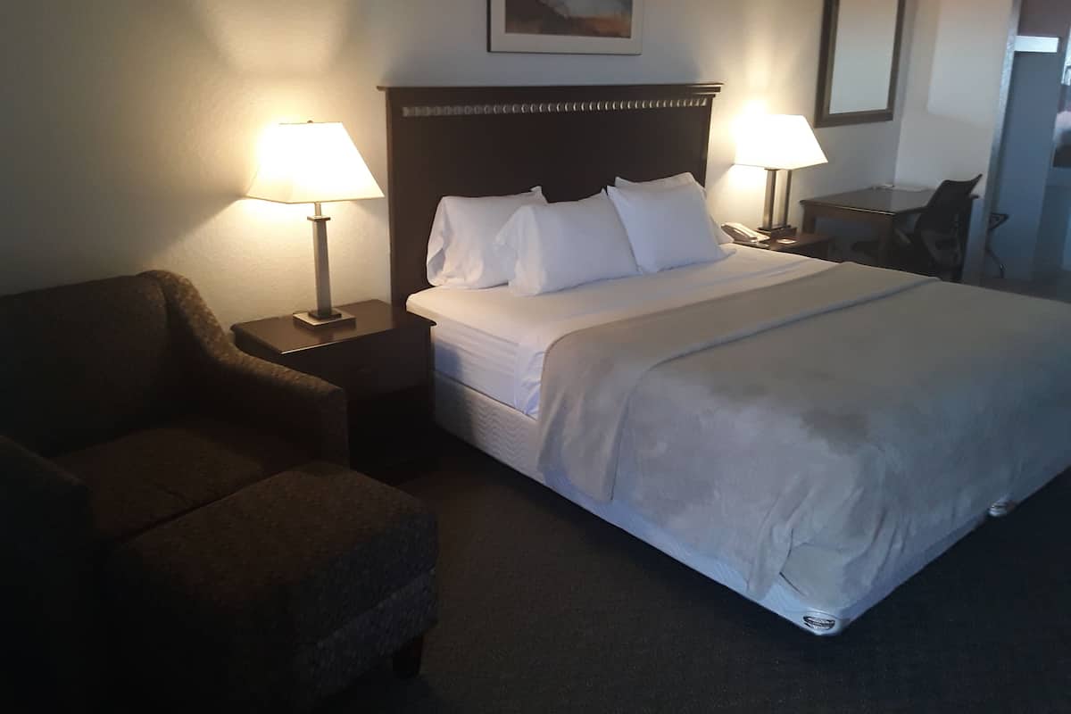 A hotel room with a bed, two bedside lamps, a chair, and a desk.