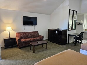 A hotel room with a sofa, a desk, a television, a mirror, and a small cabinet.
