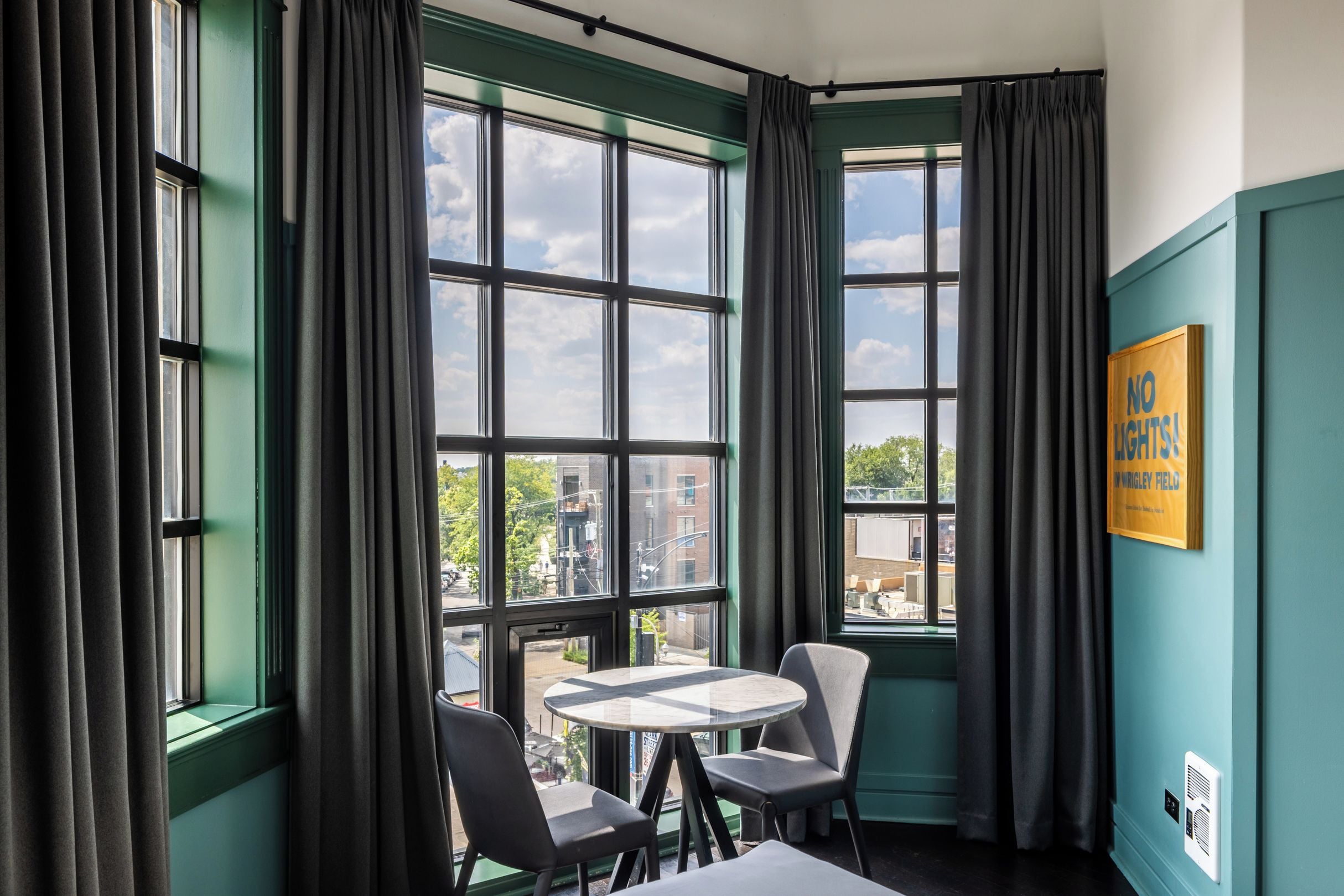 A room with a large window, a round table, two chairs, and a sign on the wall.