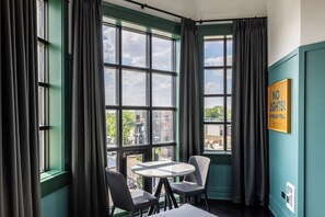 A room with a large window, a round table, two chairs, and a sign on the wall. - The Chicago Hotel Collection - Wrigleyville (Chicago)