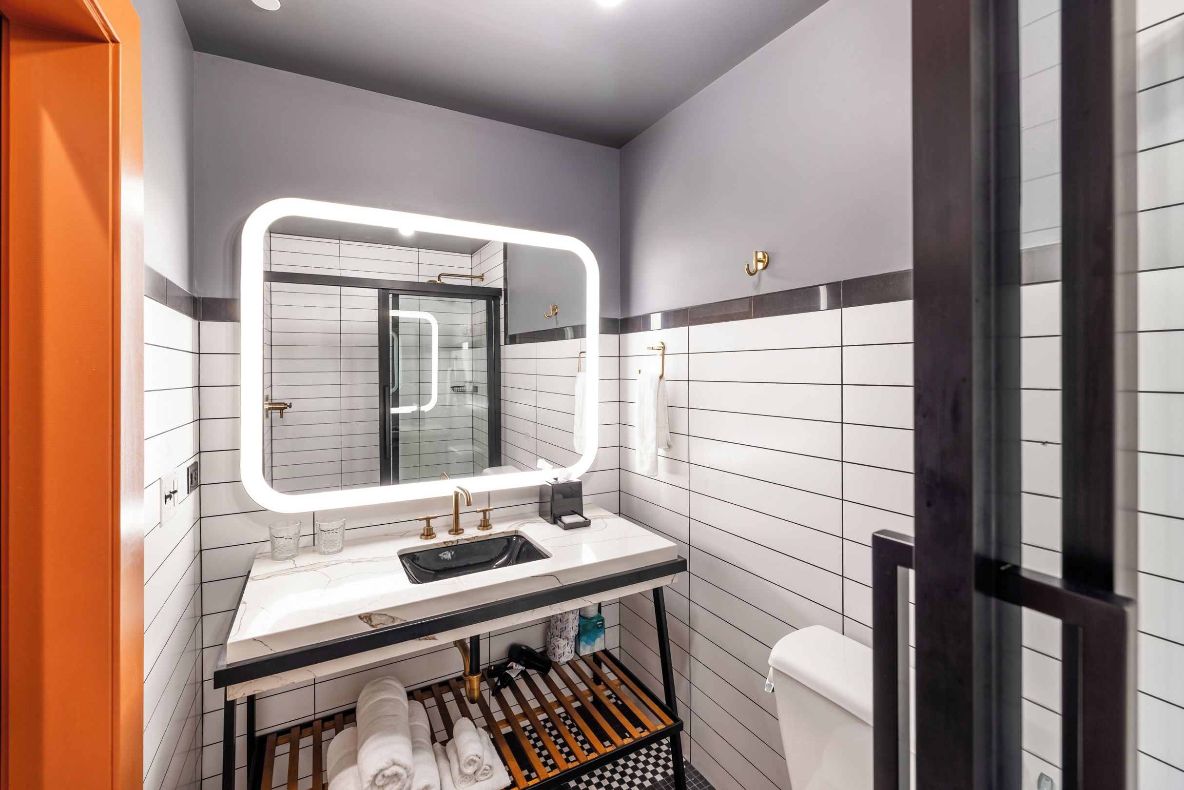 Un baño moderno con un lavabo blanco, un espejo con iluminación integrada, un perchero para toallas y un inodoro.
