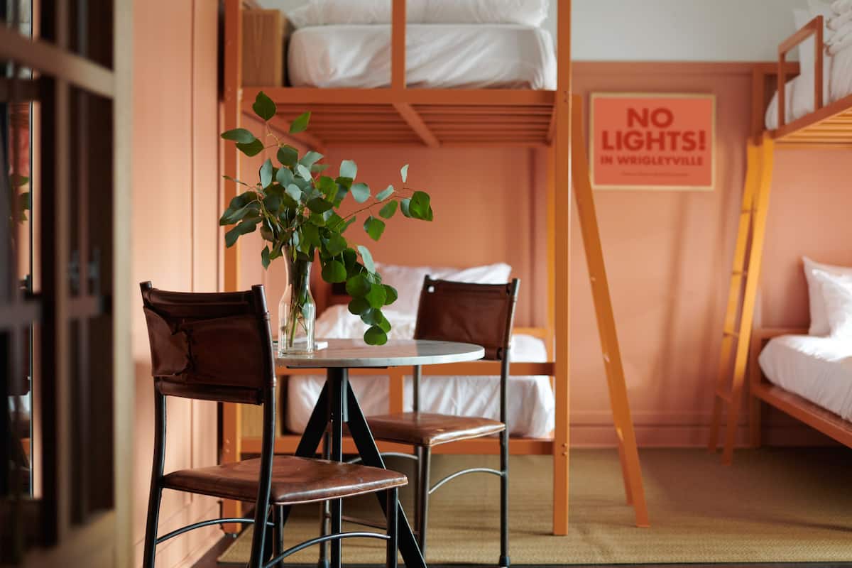 A bunk bed room with a table and chairs, a sign that says "NO LIGHTS! IN WRIGLEYVILLE", and a plant on the table.