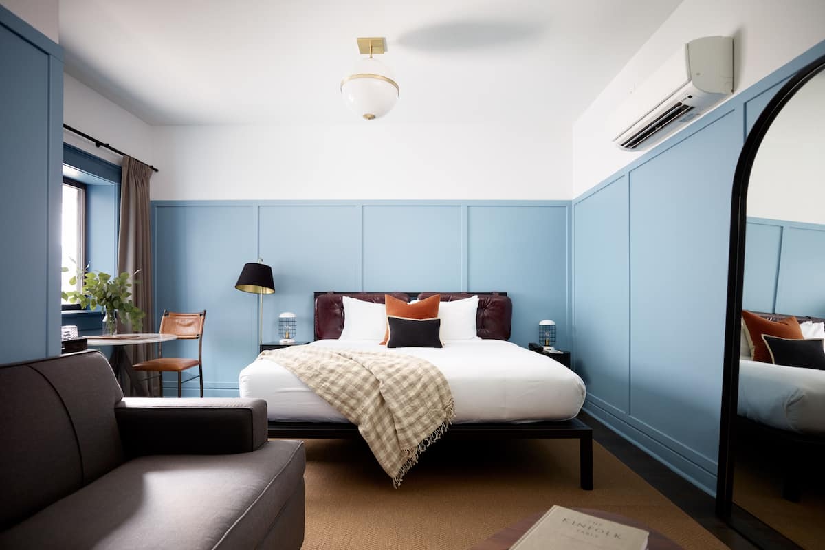 A modern hotel room with a bed, a sofa, a small table, and a mirror.