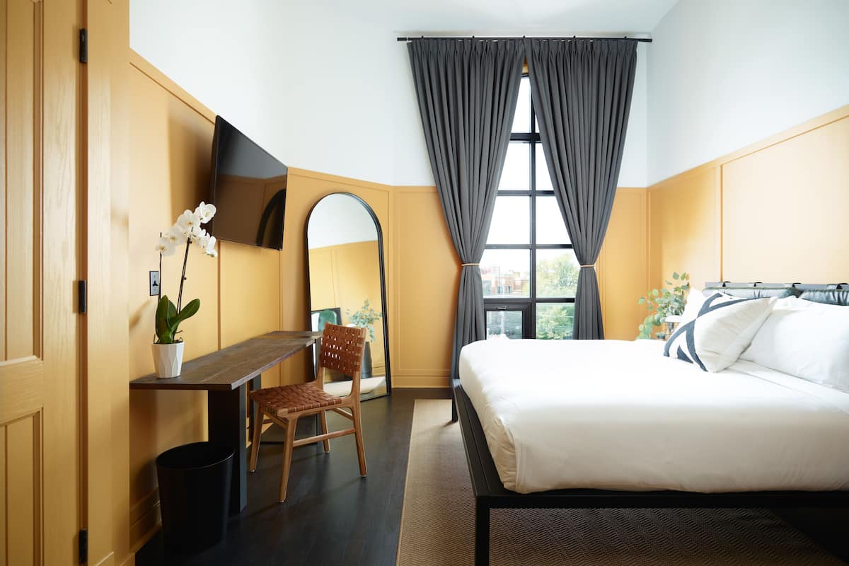 A hotel room with a bed, a desk, a chair, a TV, and a window with curtains.