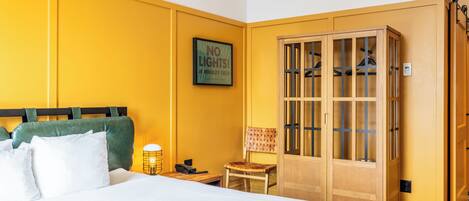 A hotel room with a bed, a wooden wardrobe, a chair, a nightstand, and a wall-mounted air conditioning unit.