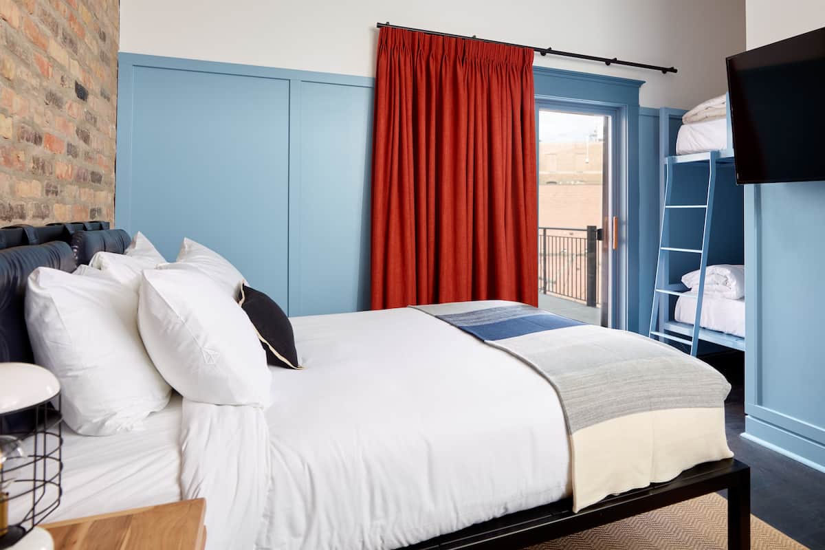 A bedroom with a bed, a bedside table, a lamp, a red curtain, a TV, and a view of the outside.