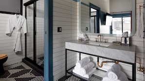 A modern bathroom with a large mirror, a marble sink, and a glass-enclosed shower.
