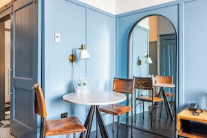 Una habitación con pared azul, una mesa redonda, dos sillas, un espejo y un teléfono.
