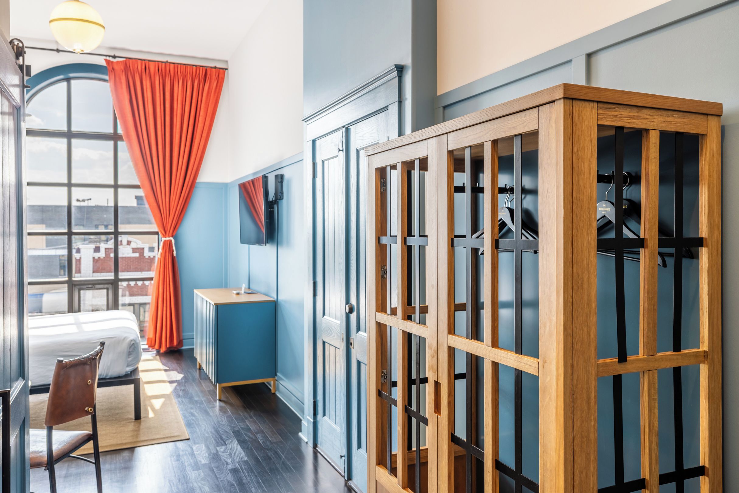 A hotel room with a bed, a desk, a wardrobe, and a window with curtains.