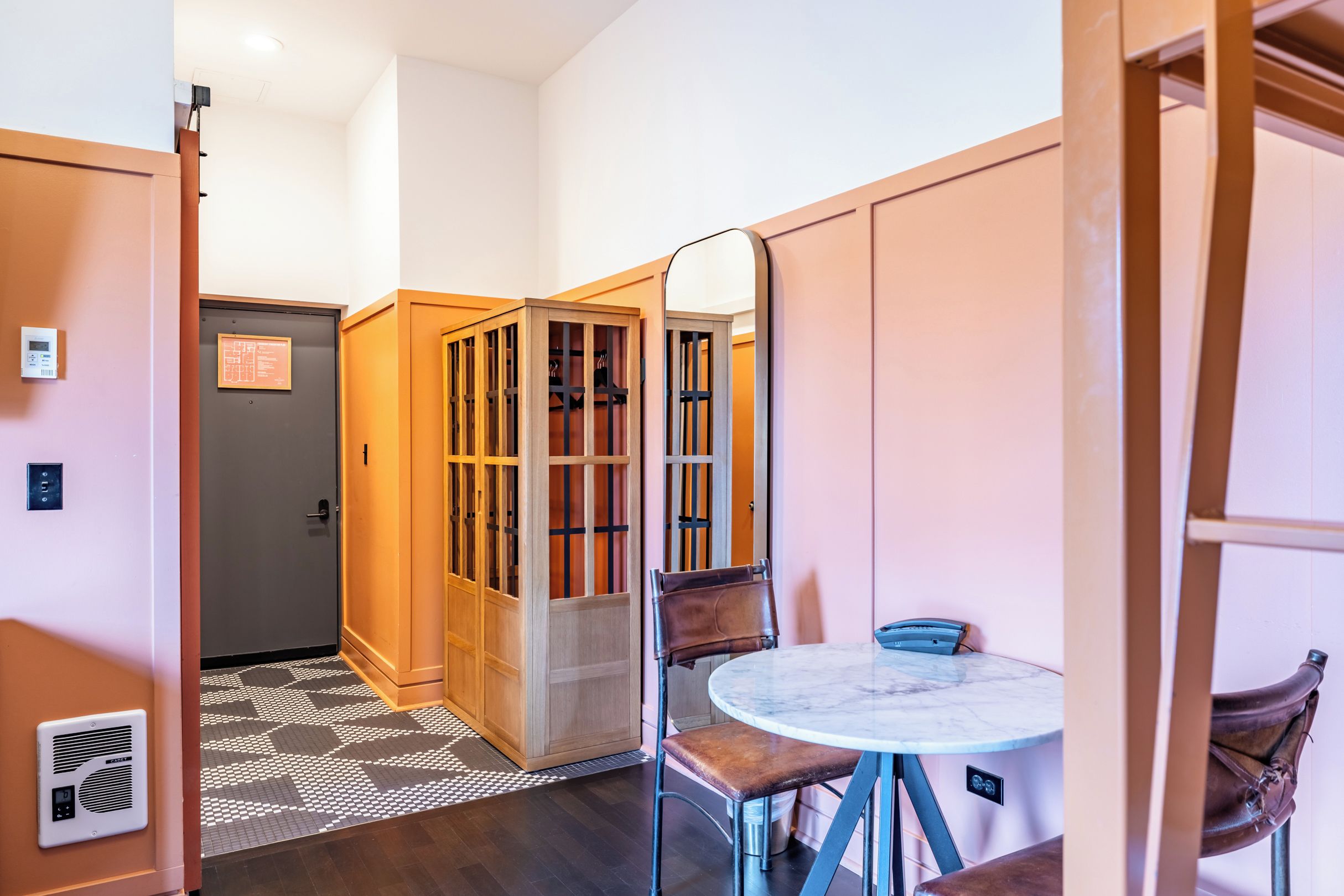 A hotel room with a wooden wardrobe, a small round table with chairs, and a patterned floor.