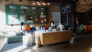 A cozy bar area with a wooden counter, cushioned seating, and a brick wall backdrop.