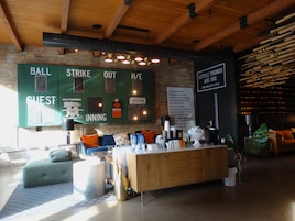 A cozy bar area with a wooden counter, cushioned seating, and a brick wall backdrop.