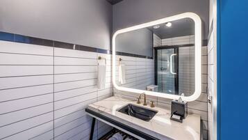 Un baño moderno con un espejo grande, paredes de azulejos blancos, encimera de mármol y un perchero para toallas.