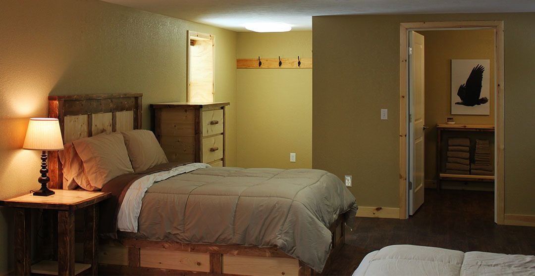 Ein Schlafzimmer mit einem Bett, einem Nachttisch mit Lampe, einer Holzkommode und einem Kleiderschrank mit Kleidung.