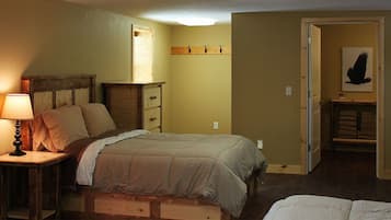 Ein Schlafzimmer mit einem Bett, einem Nachttisch mit Lampe, einer Holzkommode und einem Kleiderschrank mit Kleidung.
