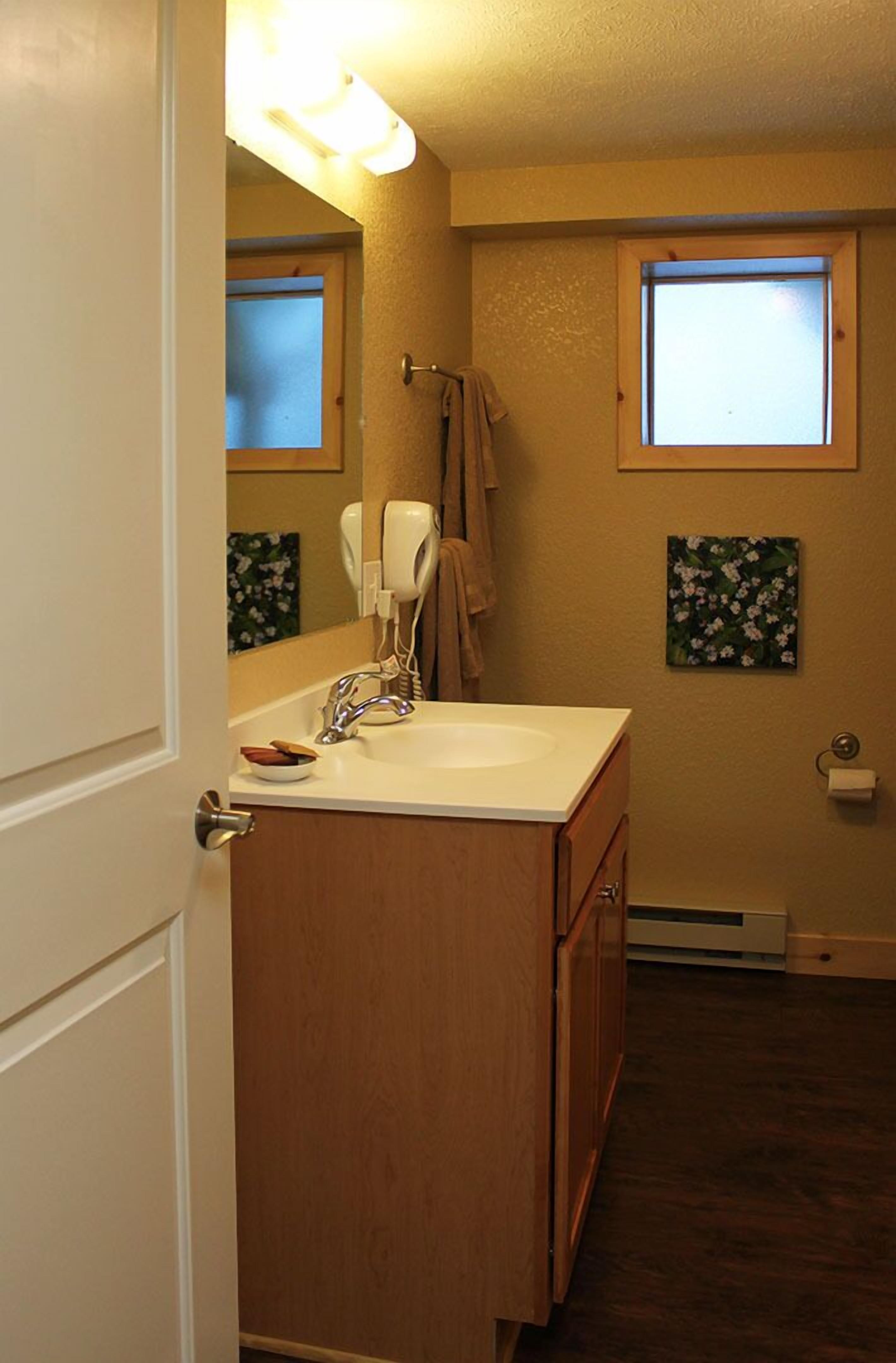 Une salle de bain avec un meuble-lavabo en bois, un lavabo blanc, un porte-serviettes et une petite fenêtre.