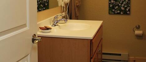 Une salle de bain avec un meuble-lavabo en bois, un lavabo blanc, un porte-serviettes et une petite fenêtre.
