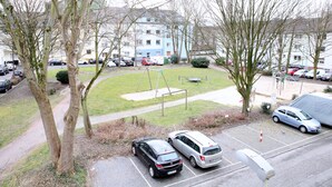 Un espace de stationnement avec des voitures, une aire de jeux et un bâtiment en arrière-plan.