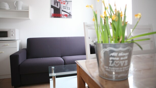 Un salon moderne avec un canapé foncé, une table basse en verre et un vase décoratif orné de fleurs.