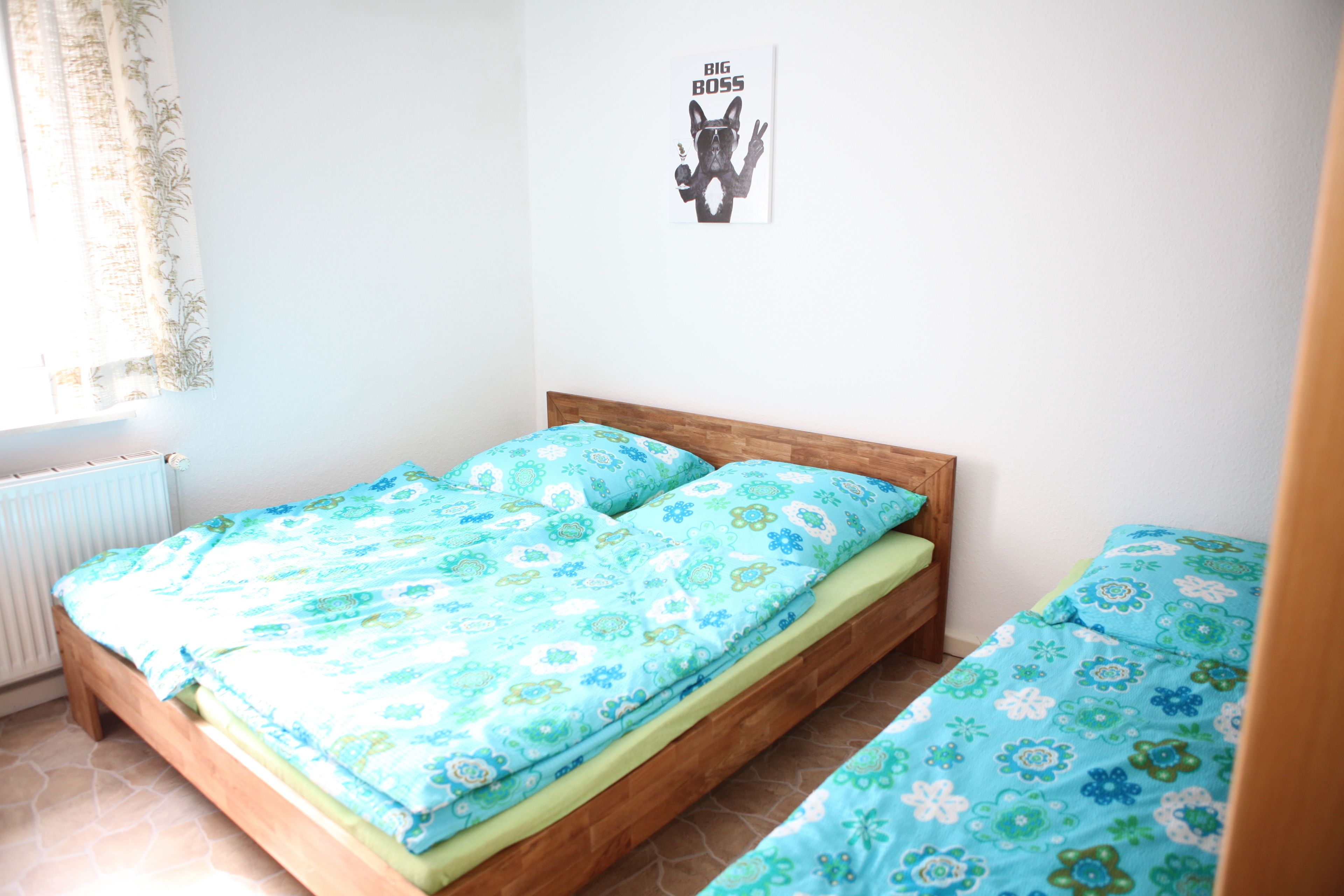 A small, tidy bedroom with a single bed, a wooden headboard, and a poster on the wall.